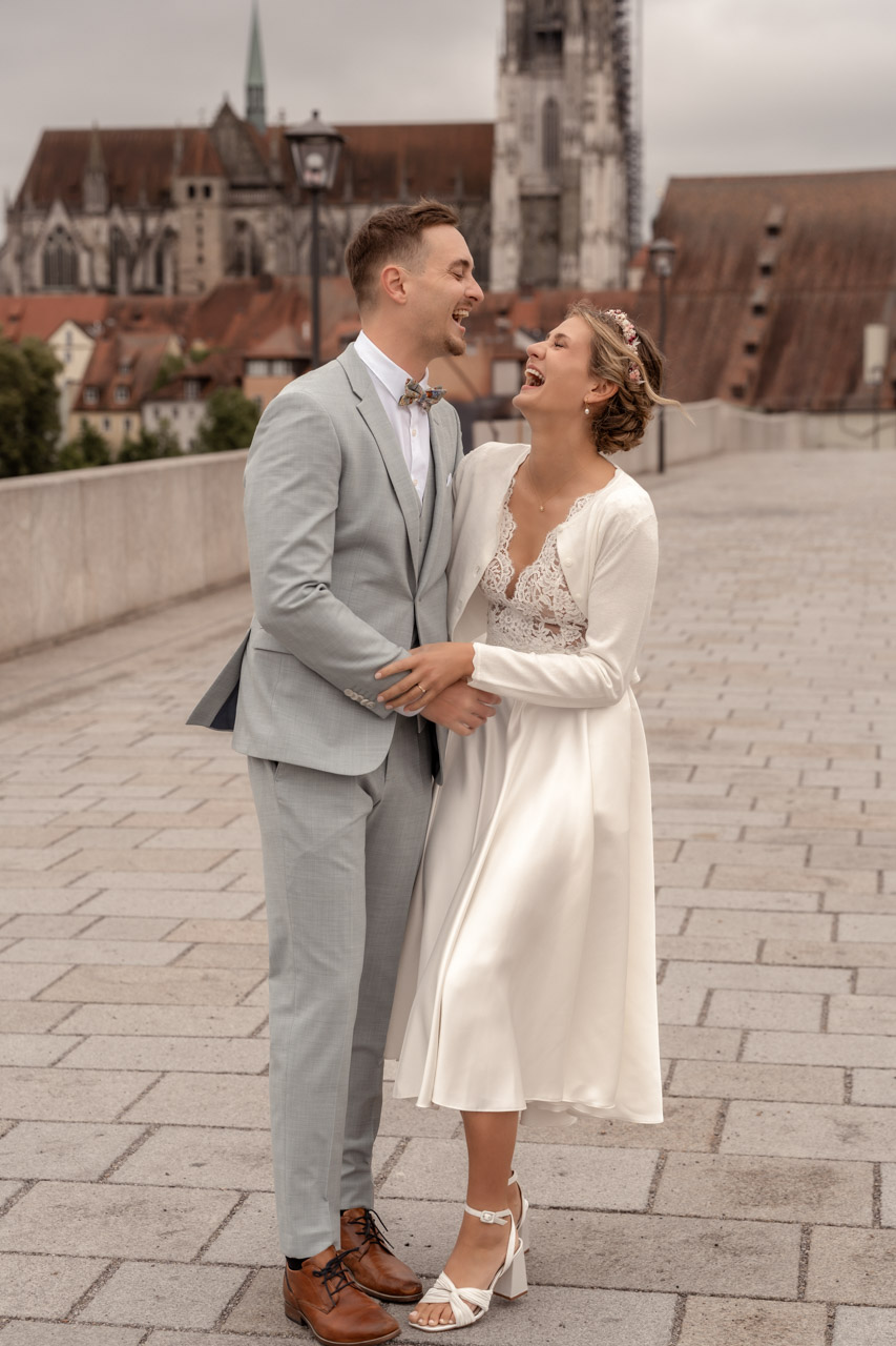 Hochzeit, Brautpaar steht auf der Steinernen Brücke in Regensburg und lacht herzlich
